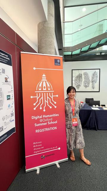 Jiayao Jiang stands next to a banner displaying the Digital Humanities Oxford Summer School logo