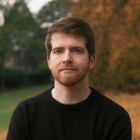 David Mahoney standing in front of trees wearing a black jumper