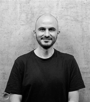 Black and white photo of Miguel standing in front of a wall, wearing a dark t shirt